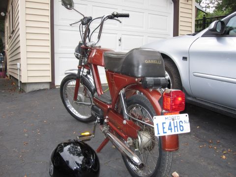 1981 Garelli Rally Sport - A red moped is parked in front of a garage, with a silver car partially visible to the right.