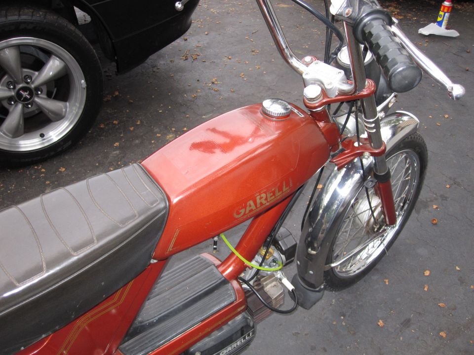 Red Garelli moped with chrome fenders and handlebars. Black seat. Part of a black car is visible on the left