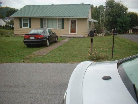 1971 Ford Ranchero - A black sedan is parked in front of a tan house with a green roof.