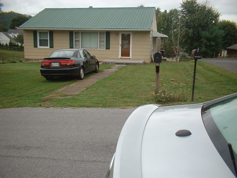 Black sedan parked on driveway, rear view. Spoiler on trunk, tinted taillights