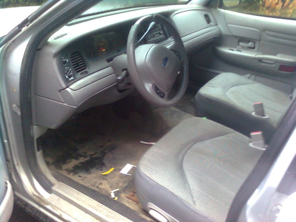 Gray Ford sedan interior seen through open driver's door, cloth seats and bare dirty floor