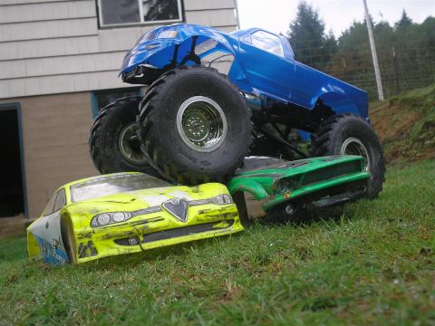 1994 Ford Escort - A blue toy monster truck is piled on top of two toy car bodies in a grassy yard.