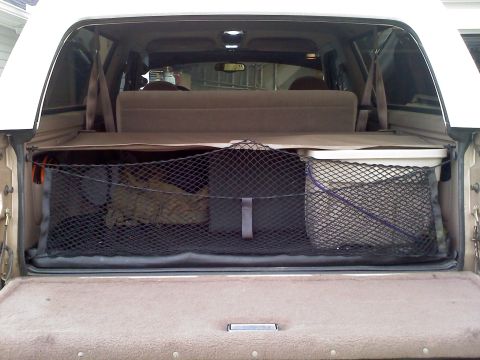 1977 Ford F-100 - The cargo area of a white SUV is organized with a net holding various items, including bags and a storage bin.