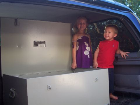 1994 Ford Bronco - Two smiling children stand in the cargo area of a vehicle, next to a large metal chest.