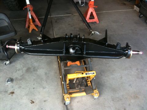 Suzuki Samurai - A black rear axle assembly is shown supported by jack stands and a hydraulic lift, likely undergoing maintenance or restoration.