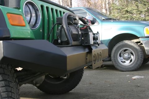 1987 Suzuki Samurai - Close-up of a green Jeep Wrangler's aftermarket bumper and winch, with a teal pickup truck visible behind it.