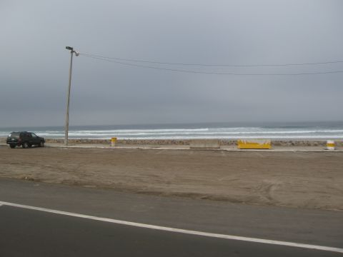 1986 Ford Bronco - A dark colored SUV is parked on a sandy area next to the ocean on a cloudy day.