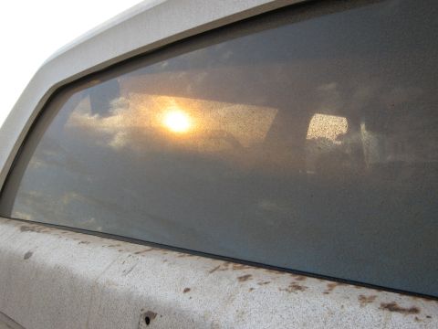 1986 Ford Bronco - The sun reflects off the dusty rear window of a vehicle, obscuring details.