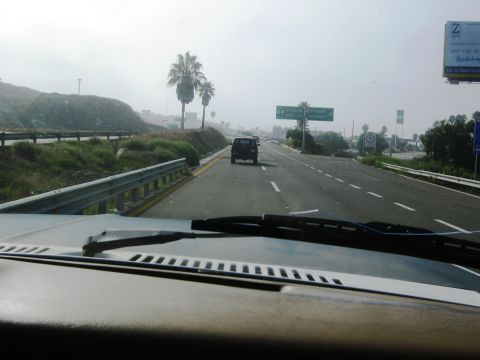 1986 Ford Bronco - A dark SUV is seen from the perspective of another vehicle on a highway with roadside vegetation and signage.