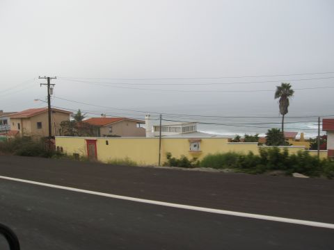 1986 Ford Bronco - View of houses and the ocean from a road, with a prominent yellow wall and a single palm tree.