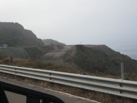 1986 Ford Bronco - View from a vehicle traveling along a scenic coastal highway with mountains on one side and the ocean on the other.
