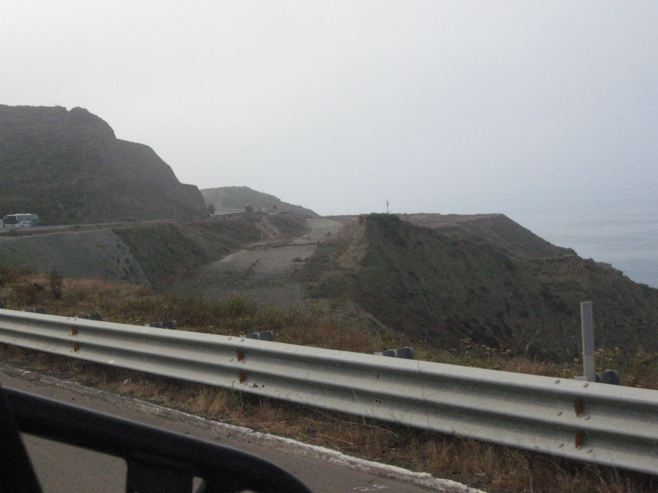 Coastal highway with guardrail and distant mountains under a hazy sky