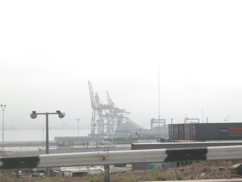 1986 Ford Bronco - A hazy view of industrial shipping cranes and stacked containers at a port facility.