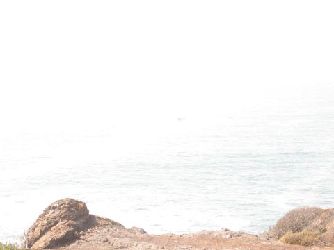 1986 Ford Bronco - A distant boat sails on the ocean, with a rocky shore visible in the foreground.
