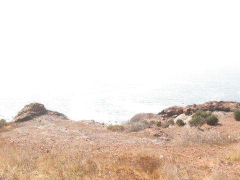 1986 Ford Bronco - A wide view of a coastal landscape with rocks and the ocean under a hazy sky.