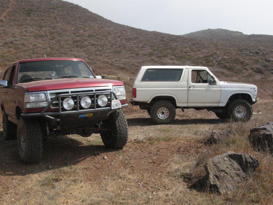 Red Ford Bronco with custom bumper and lights, white Ford Bronco in background