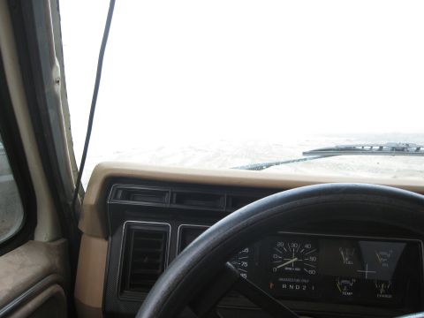1986 Ford Bronco - Interior view of a vehicle's dashboard and steering wheel, with a bright, overcast sky visible through the windshield.
