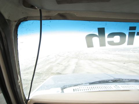 1986 Ford Bronco - View from inside a vehicle shows a snowy terrain through the windshield, with partial text on the glass.