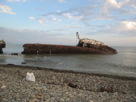 1986 Ford Bronco - Shipwreck on a rocky shore under a cloudy sky.