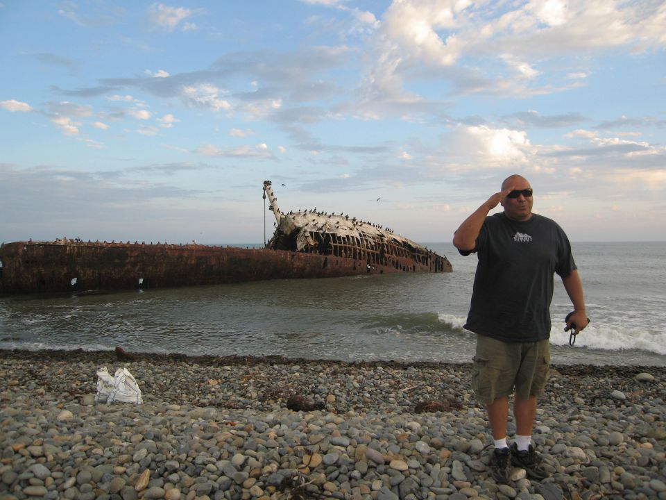 Man salutes near a beached shipwreck on a rocky shore