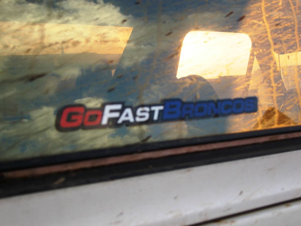 GoFastBroncos sticker on a dirty vehicle window, reflecting sky and clouds