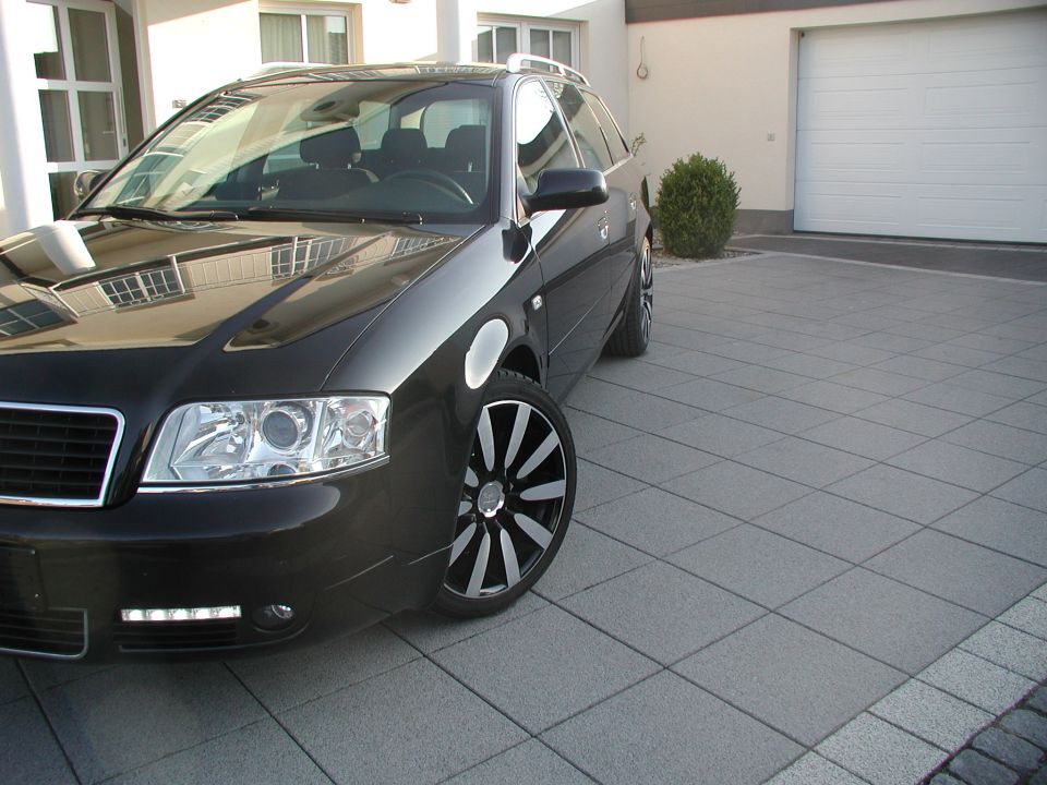 Black Audi A6 Avant wagon parked on paved driveway, front three-quarter view with alloy wheels.