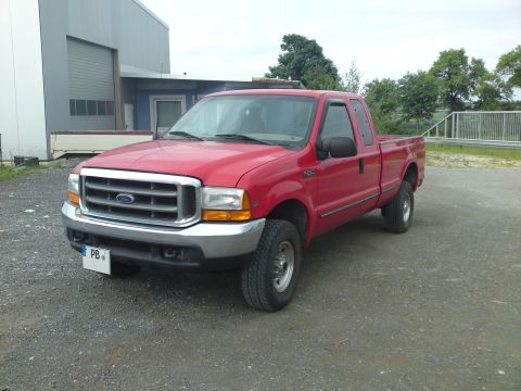 1999 Lincoln Town Car - This red Ford F-250 Super Duty pickup truck is parked on a gravel lot near a large industrial building.
