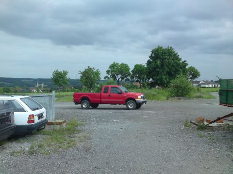 1999 Lincoln Town Car - A red pickup truck is parked in a gravel lot with other vehicles visible.