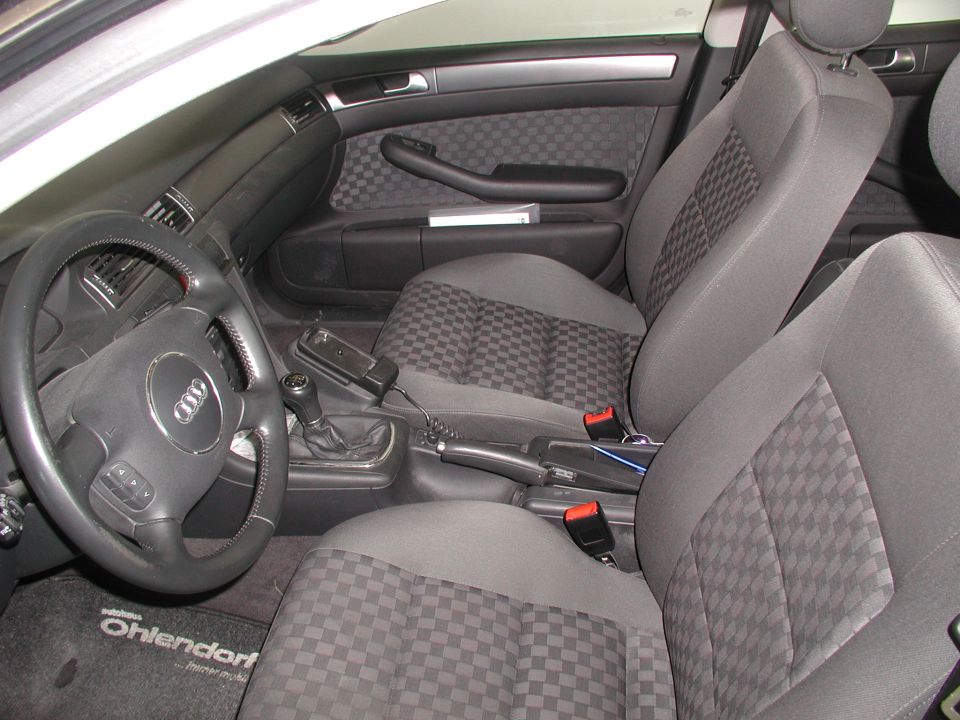 Driver's side interior of a 2003 Audi A6, showing the steering wheel, dashboard, center console, and front seats with checkered fabric inserts