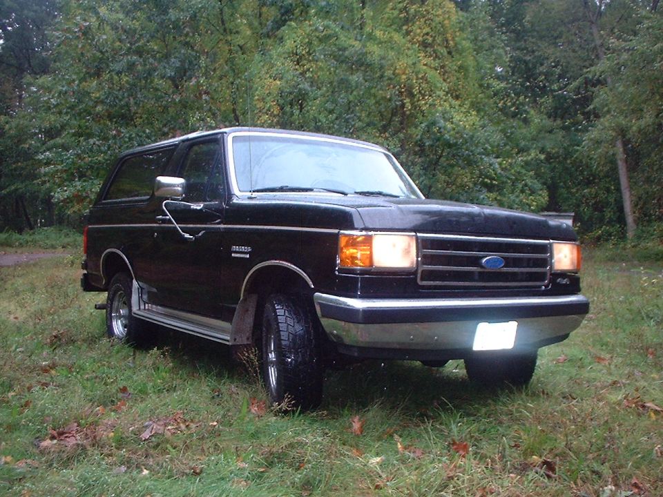 Black Ford Bronco parked on grass, front 3/4 view. Chrome trim and grille visible