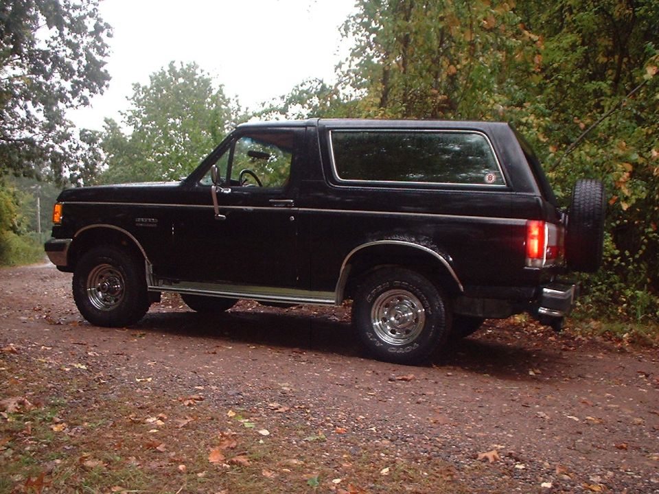 Black 1989 Ford Bronco parked on a dirt road with trees in the background