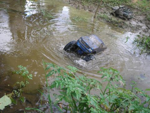 1994 Ford Escort - A blue remote control car struggles in the mud, while another RC vehicle navigates the terrain in the background.
