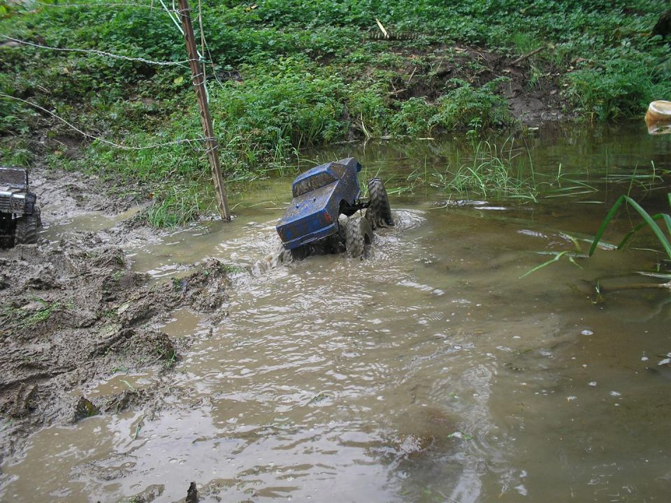 Blue toy RC truck stuck in muddy water, another toy truck visible to the left