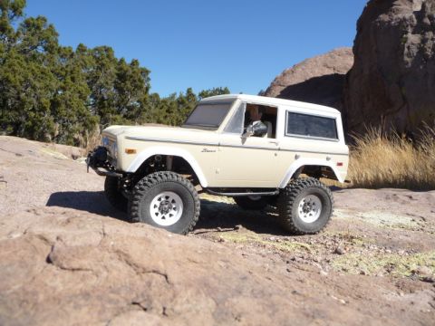 1988 Ford Bronco - This vintage Ford Bronco, likely from the early 1970s, navigates a , rocky landscape under a clear blue sky.