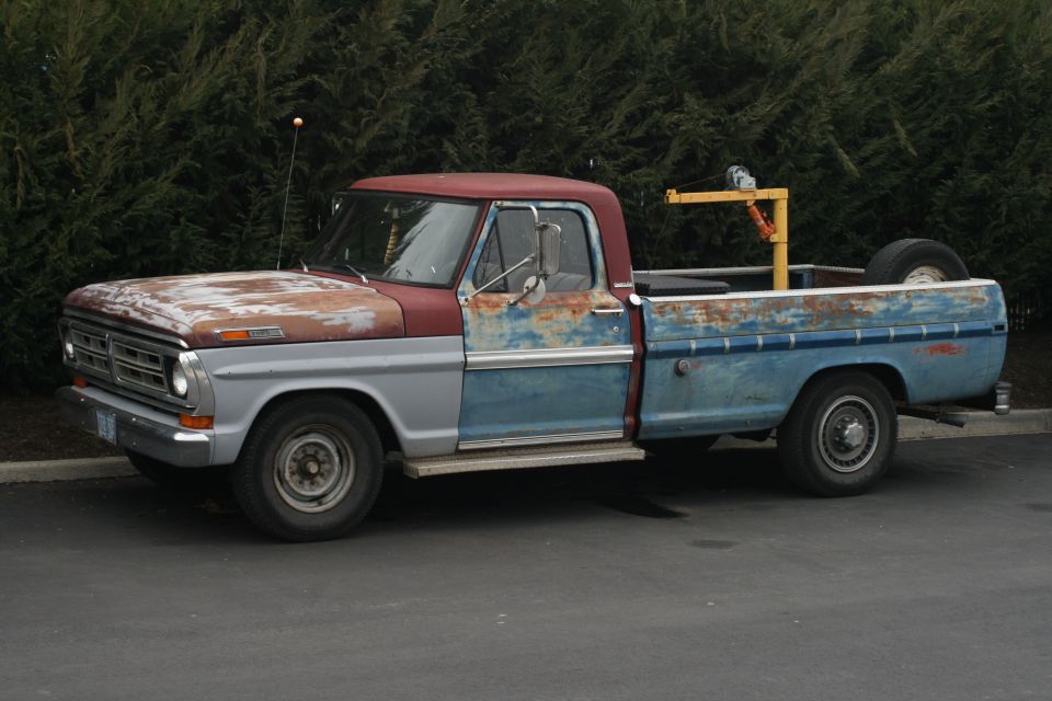 1967 Ford F-250 truck, side view, showing rust and mismatched paint colors. A yellow crane is mounted in the truck bed