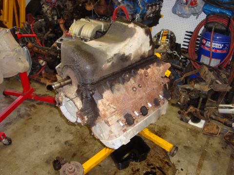 1989 Ford Bronco - A heavily used engine block sits on a stand in a cluttered garage, surrounded by spare parts and other engines.