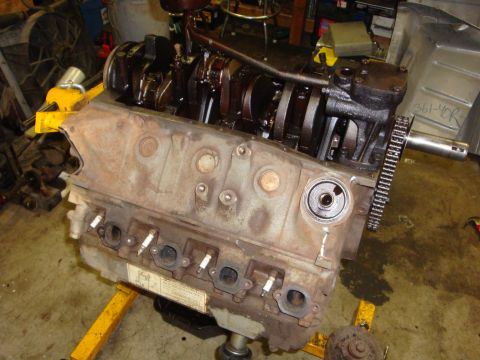 1989 Ford Bronco - Close-up of an engine block, showing the crankshaft and spark plug holes, resting on a yellow engine stand.
