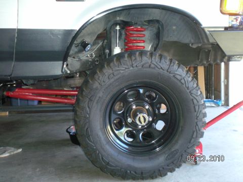 1996 Ford Bronco - This image shows the side of a white truck, focusing on its lifted suspension system with prominent red springs and control arms.