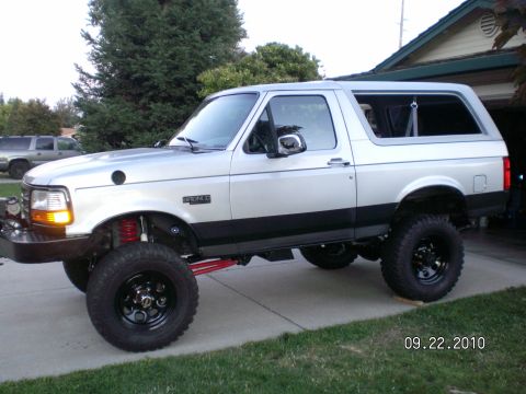 1996 Ford Bronco - A silver 1996 Ford Bronco with a lifted suspension and black trim is parked on a driveway next to a house.