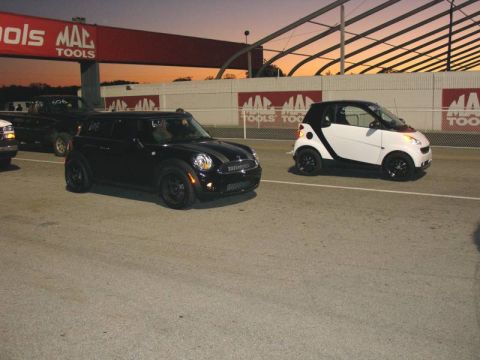 2010 MINI Cooper - Two small cars, a black MINI Cooper and a white Smart car, are parked side-by-side on asphalt.