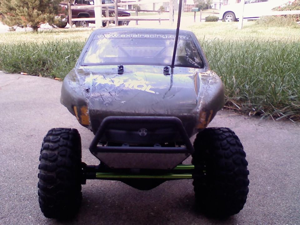Front view of a scratched olive-drab Axial RC rock crawler with green links and knobby tires on a driveway