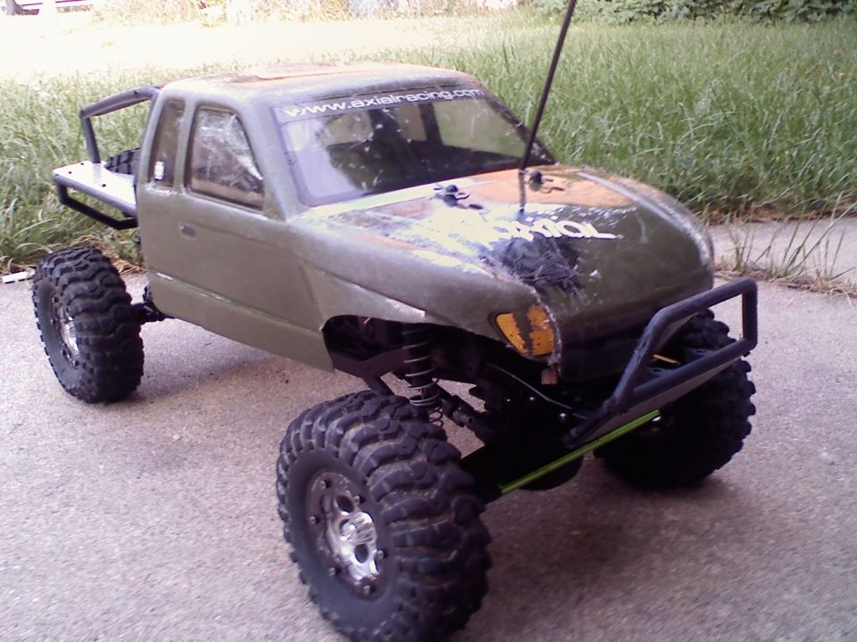 Olive-drab RC rock crawler truck with big knobby tires and tube cage on a driveway