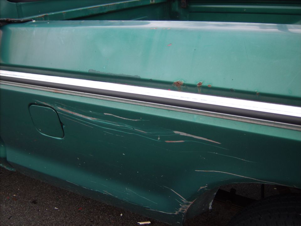 Green 1979 Ford F-250 bed side panel with chrome trim, gas cap door, scratches, and rust spots