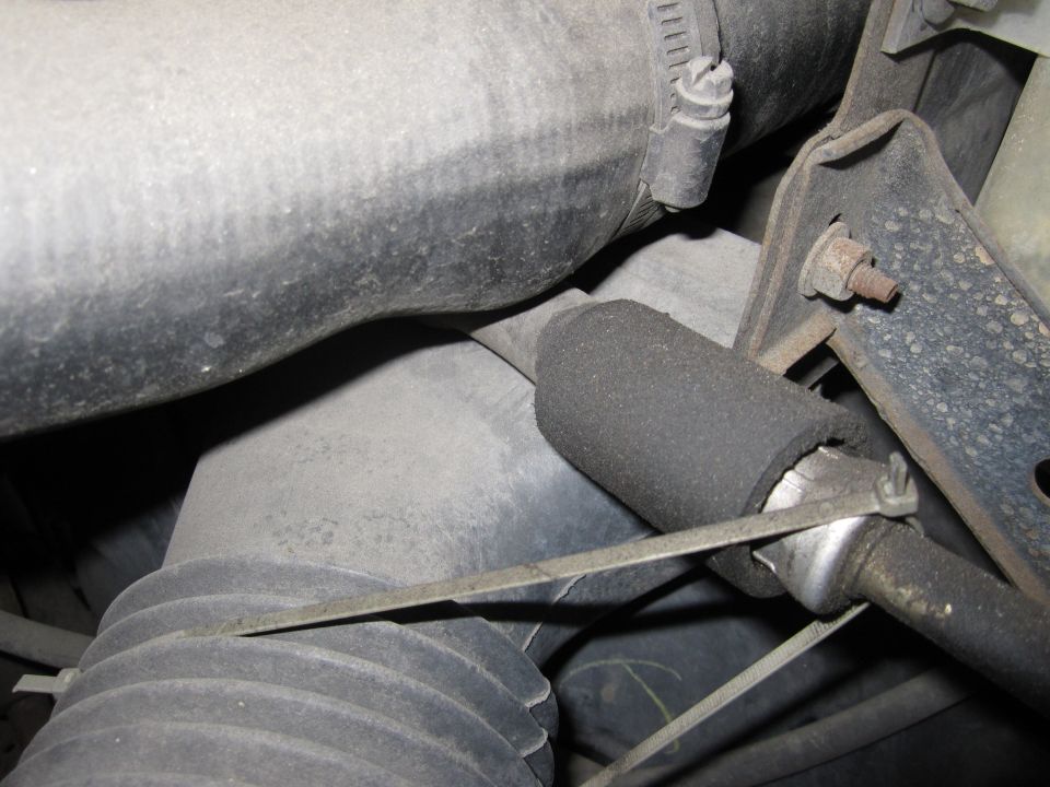 Engine bay close-up of black rubber intake ducting, hose clamps and foam-wrapped vent tube