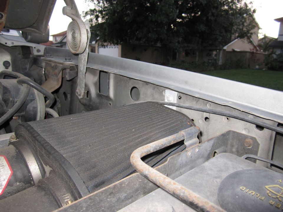 Under-hood view of black cooler core, rusty prop rod and radiator core support