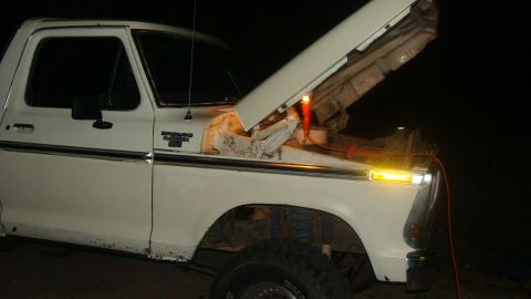 1978 Ford Bronco - The hood of a white Ford Bronco is open at night, revealing the engine and jumper cables.