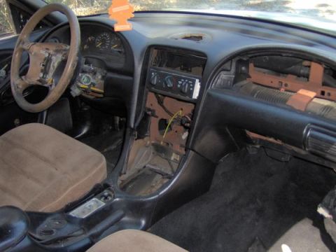 1994 Ford Mustang - The interior of a 1994 Ford Mustang shows worn tan seats and a damaged dashboard.