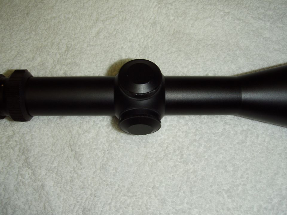 Black rifle scope with turrets and adjustable objective lens, on a textured surface