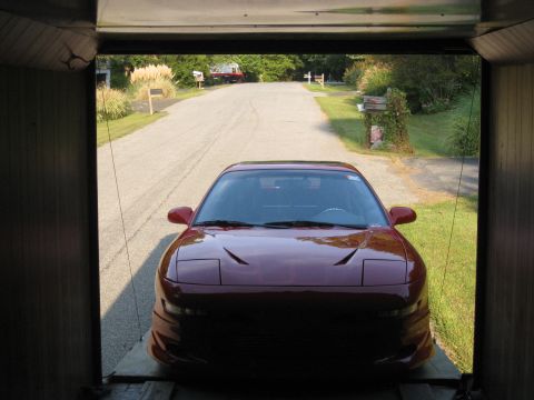 1994 Ford Probe - A red coupe with pop-up headlights is positioned inside a garage, facing outwards towards a suburban street.
