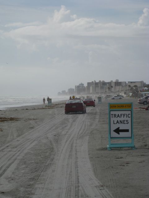 1994 Ford Probe - A sign indicates traffic lanes on a beach road, with cars driving along the shore.